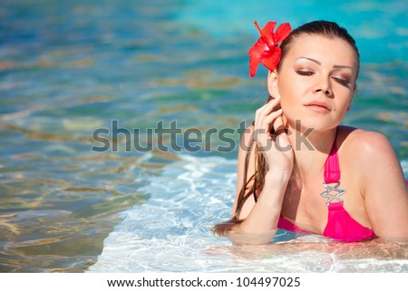 Beautiful young woman with flower resting in the pool of expensive hotel
