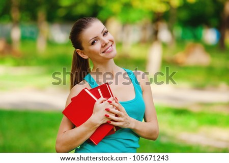 Young student holding books stands in summer park outdoor