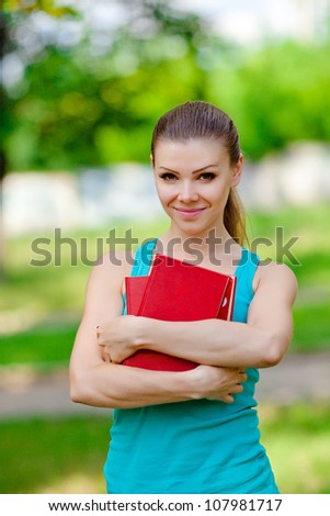 Young student holding books stands in summer park outdoor