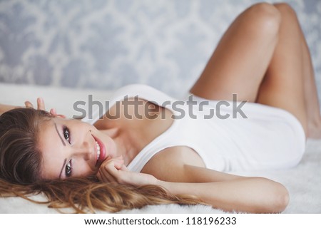 A beautiful smiling woman resting on white bed - stock photo