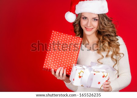 Santa girl holding christmas gift. Young happy woman in santa hat looking sideways showing Christmas present isolated on white background. Beautiful cute young santa woman.