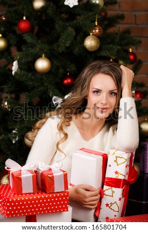 Happy young woman sitting near christmas tree with pile of present boxes around