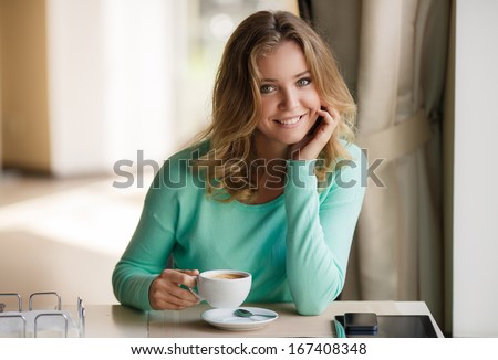 Portrait Of A Cute Blonde Smiling Woman Sitting In A Cafe With A Cap Of Coffee