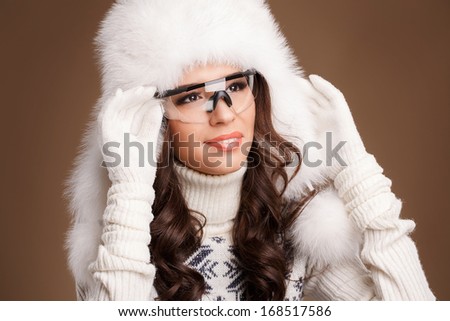 Portrait of a happy pretty young woman in winter fury hat and winter glasses on brown background