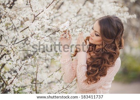 portrait of Beautiful young brunette woman standing near blooming trees in spring garden