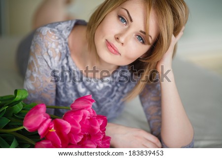Beautiful young blond woman with tulip bouquet. Spring portrait. Bright pink flowers in girl\'s hands. At home. Interior portrait/