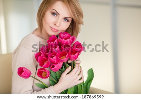 portrait of Beautiful blonde woman with the bouquet of pink tulips in interior background