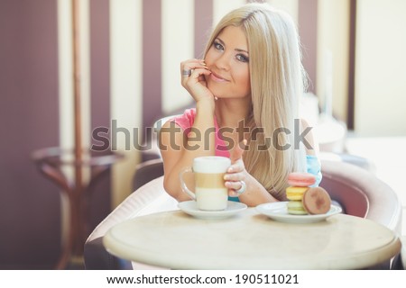 Cafe city lifestyle woman drinking coffee sitting indoor in trendy urban cafe. Cool young modern Caucasian blonde female model in her 20s. Portrait close up