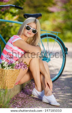 Beautiful young blonde woman with bicycle in Countryside, Summer Lifestyle. Blooming Flowers around