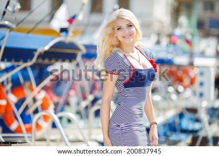 Beautiful sexy blonde woman wearing sailor striped dress posing near boats