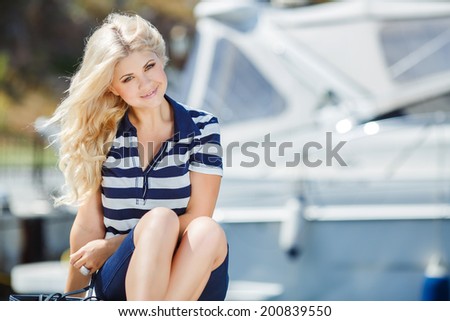 Adorable blonde woman wearing sea shorts and sexy sailor T-shirt sitting on yachts background and the sea