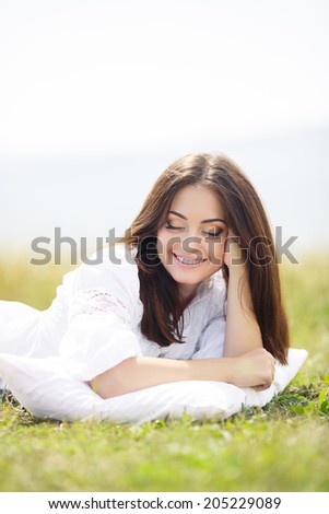 Young cute girl resting on soft pillow in fresh spring grass. Young woman sleeping on soft pillow in fresh spring grass.