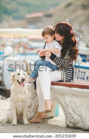 Happy mother and son sitting on the quay with dog. happy mother playing with her son near the sea playing with the dog