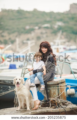 Happy mother and son sitting on the quay with dog. happy mother playing with her son near the sea playing with the dog
