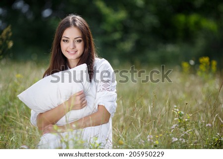 Young cute girl resting on soft pillow in fresh spring grass. Young woman sleeping on soft pillow in fresh spring grass. smiling woman portrait outdoors.