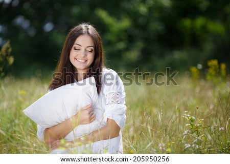 Young cute girl resting on soft pillow in fresh spring grass. Young woman sleeping on soft pillow in fresh spring grass. smiling woman portrait outdoors.