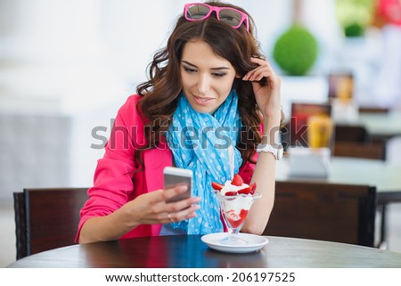 young beautiful woman eating a dessert. Image of young female reading sms on the phone in cafe. Cute young woman in cafe restaurant with phone