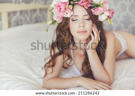 beautiful woman portrait with wreath of flowers on head laying on bed in light bedroom