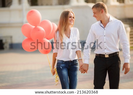 summer holidays, celebration and dating concept - couple with colorful balloons in the city. Young couple kissing among white columns and holding bunch of balloons