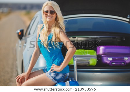 Travel, tourism - Girl ready for the travel for summer vacation. Young female sitting in the trunk of a car with suitcases, showing thumb up sign, ready to leave for vacations