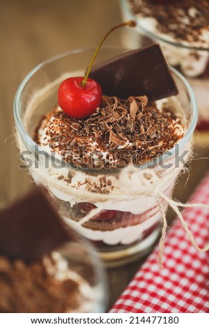 Glasses with cherries and chocolate parfait with whipped sour cream. Shallow dof. Delicous redcurrant sundaes or desserts? glasses of colorful layered berry coulis, ice cream or frozen yoghurt