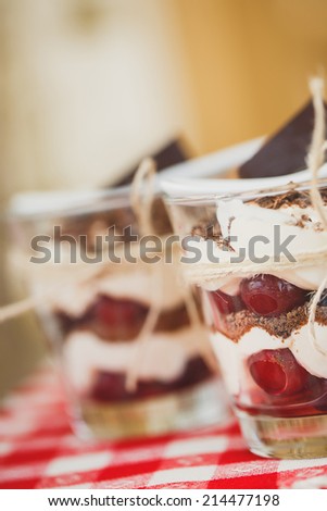 Glasses with cherries and chocolate parfait with whipped sour cream. Shallow dof. Delicous redcurrant sundaes or desserts? glasses of colorful layered berry coulis, ice cream or frozen yoghurt