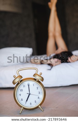 Great alarm clock in the foreground. Close up image of alarm clock over the blurred sleeping woman.sleepy woman waking up and yawning with a stretch while sitting in bed