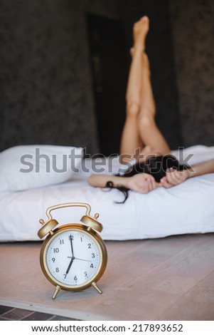 Great alarm clock in the foreground. Close up image of alarm clock over the blurred sleeping woman.sleepy woman waking up and yawning with a stretch while sitting in bed
