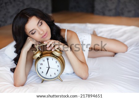 Young woman with alarmclock on the bed at the morning. Relaxed beautiful young woman sleeping in bed at home.