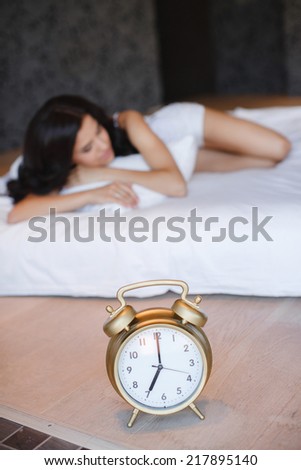 Relaxed beautiful young woman sleeping in bed at home. Woman sleeping in bed. Alarm clock in focus in foreground.
