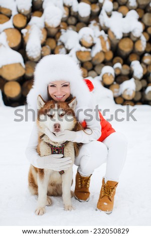 Happy young woman playing with siberian husky dogs in winter forest. Beautiful girl hugging the dog. The girl with the siberian husky