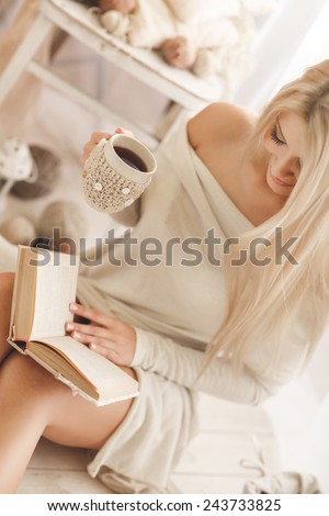 Soft photo of woman on the bed with old book and cup of coffee in hands, top view point. Cozy, comfy, soft. Pretty young woman enjoying reading a book at home, smiling in pleasure in casual clothing.