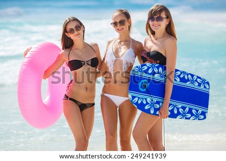 Beautiful women in bikini at the seaside. Joyful team of friends having fun at the ocean beach. Four slim young girls in bikinis on the beach enjoying the sun and blue water.