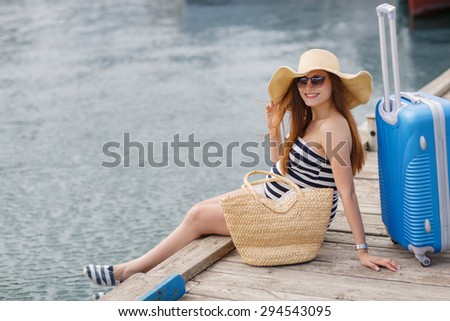 Pregnant beautiful woman by the sea with summer straw hat? sunglasses and suitcase. Vacation concept