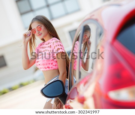 young woman with long hait standing near her red car. woman with car outdoors