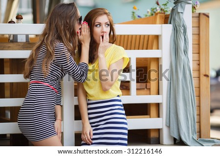 Two girl friends whispering secrets. summer holidays and vacation concept - girls gossiping . friendship, gossip and happiness concept - one girl telling another secret