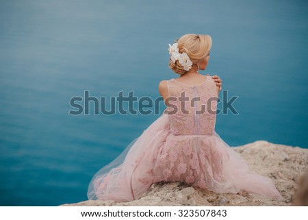 Beautiful bride posing on the coast with angelic dress. Bride in wedding dress stands on a cliff with a beautiful sea view from the top. Beautiful bride by the sea