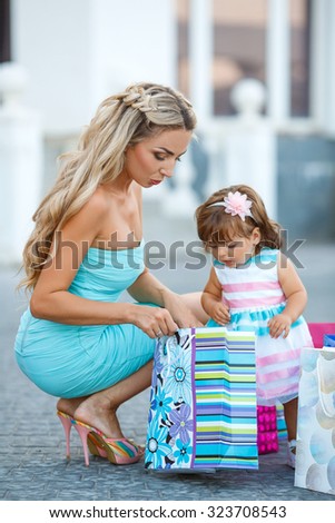 Young mother and her daughter doing shopping together. Woman with child on shopping in shopping mall with bags. Mother with baby girl with shopping bags with mall on background. Fashion and beauty.