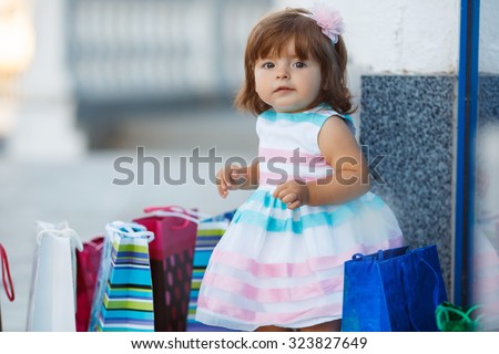 Child with shopping bags. Young girl with full of bags. Cute baby goes shopping with bags, shops in background. A little girl with the packages in the shop.Beautiful shopping girl in store
