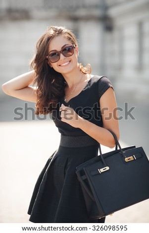 Woman in classic black dress, hills and bag sitting on stairs in the city street. woman portrait outdoor in summer