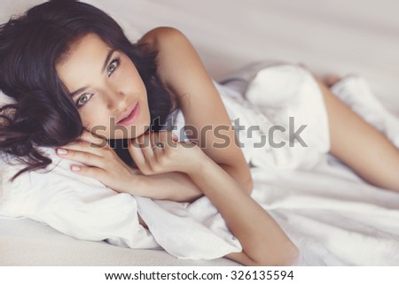 A woman lying at the end of the bed, with her head resting upon a pillow.