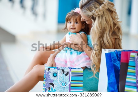 Family shopping. Young mother and her daughter doing shopping together. Woman with child on shopping in shopping mall with bags. Mother with baby girl with shopping bags with mall on background.