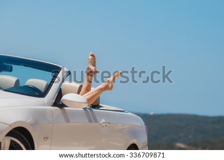 Women\'s legs against blue sea and sky background. Summer vacations concept. Woman relaxing in a car. fashion photo of beautiful sexy girl\'s legs  posing in luxury cabriolet on sun