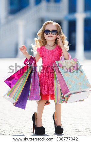 cute little girl on shopping. portrait of a kid with shopping bags. child in dress, sunglasses and shoes near shopping mall having fun. shopping. girl.