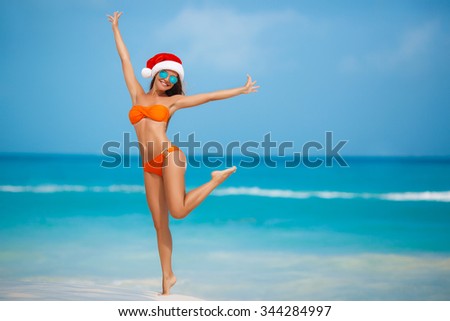 Young woman in santa hat sitting on beach. Christmas vacation. Christmas beach vacation travel woman wearing Santa hat and bikini enjoying christmas on tropical beach. woman in santa hat and bikini