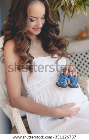 Small shoes for the unborn baby in the belly of pregnant woman. sneakers on belly. Pregnant woman holding small baby shoes relaxing at home.