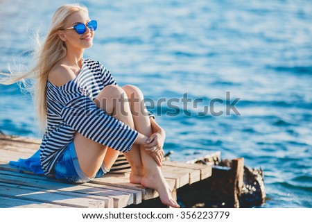Beautiful Girl in sea style sitting on wooden bridge. Travel and Vacation. Freedom Concept. Sensual blonde beautiful woman, Girl with perfect body and long healthy hair,Marine style