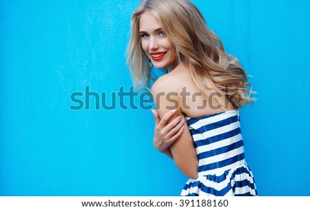 beauty fashion portrait of blonde woman with red lips and stripped dress. Fashion portrait. Smiling blonde woman in fashionable look. Sea style. On blue background. Style and hot girl outdoor.