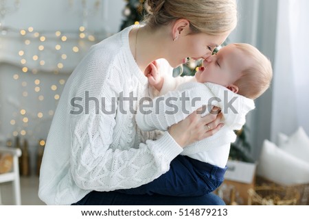 happy family mother and baby little son playing home on Christmas holidays. New Year\'s holidays. Toddler with mom in the festively decorated room with Christmas tree. Portrait of mother and baby boy