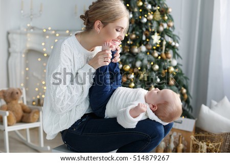 happy family mother and baby little son playing home on Christmas holidays. New Year\'s holidays. Toddler with mom in the festively decorated room with Christmas tree. Portrait of mother and baby boy